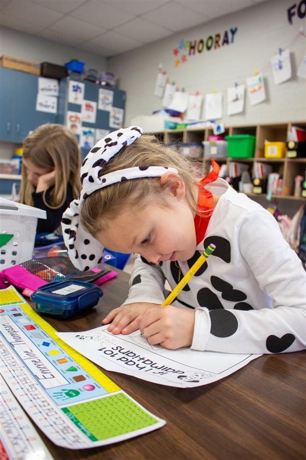 girl dressed as dalmatian dog writing on paper